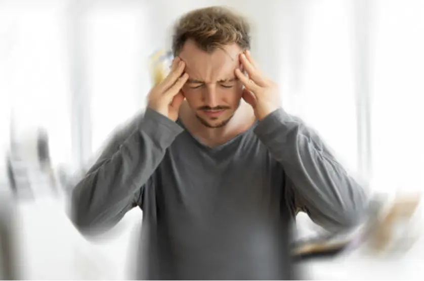 A man holds his head and rubs temples, looking stressed or in pain indoors.