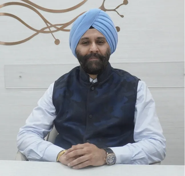 essen Picture 7 | Gurneet A bearded man wearing a blue turban and navy vest sits at a desk, hands folded, smiling gently.