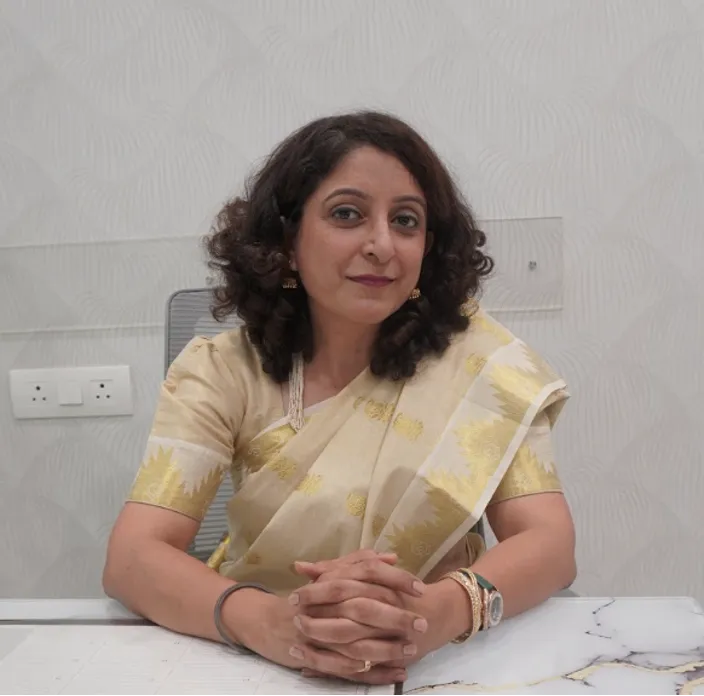Cardiac Rehabilitation Therapy in Mumbai Picture 4 | Gurneet Woman in a cream and gold saree sits at a desk with hands folded, looking at the camera.